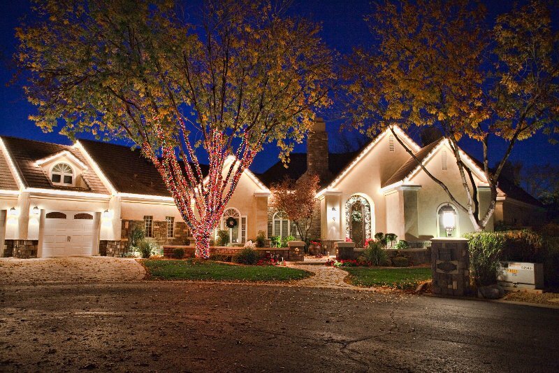 Warm white Christmas lights along the rooflines and wrapped trees of a Tempe AZ home at dusk