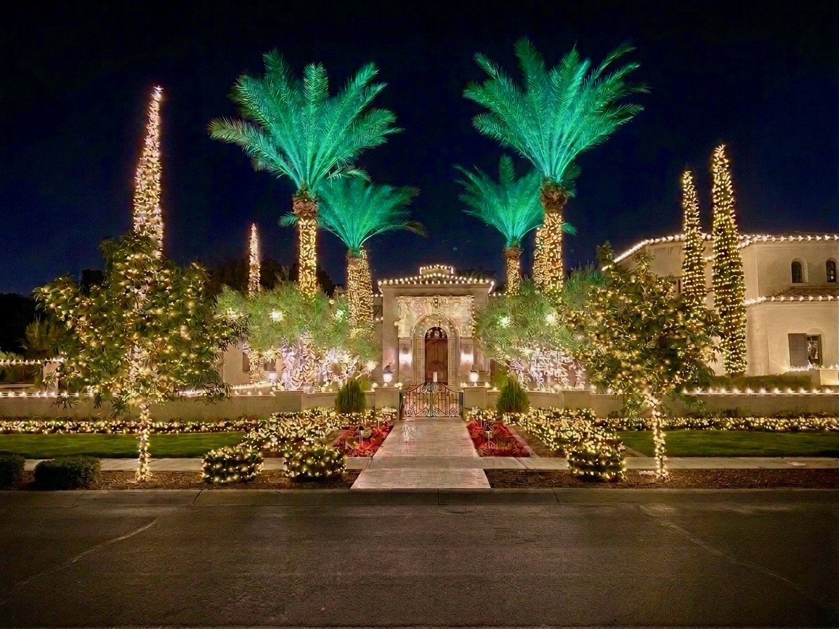 Christmas lights with green-lit palms and warm white roofline on a Phoenix Mediterranean estate at night