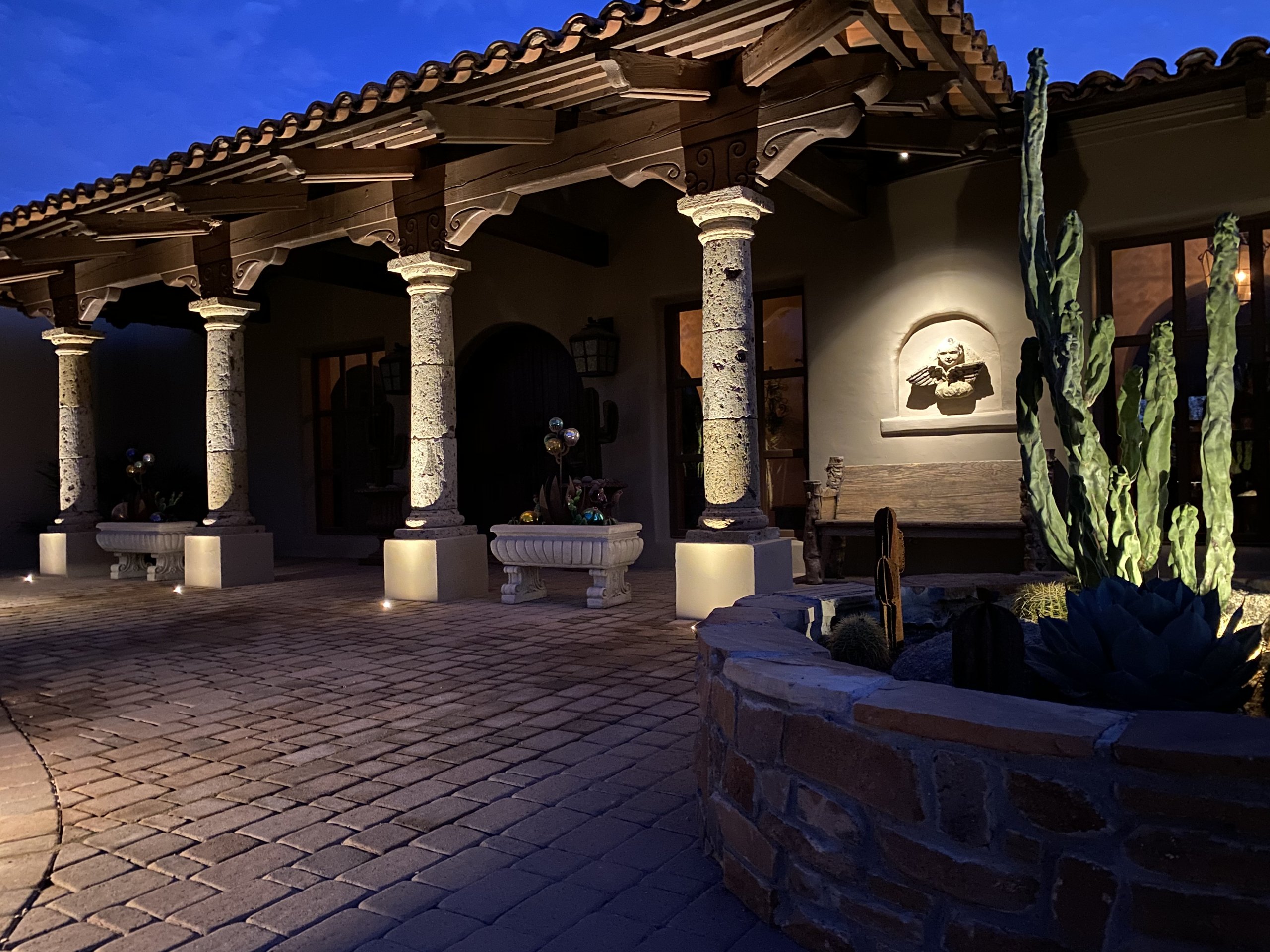 Landscape lighting uplighting stone columns and a tiled courtyard at a Phoenix Mediterranean home at dusk
