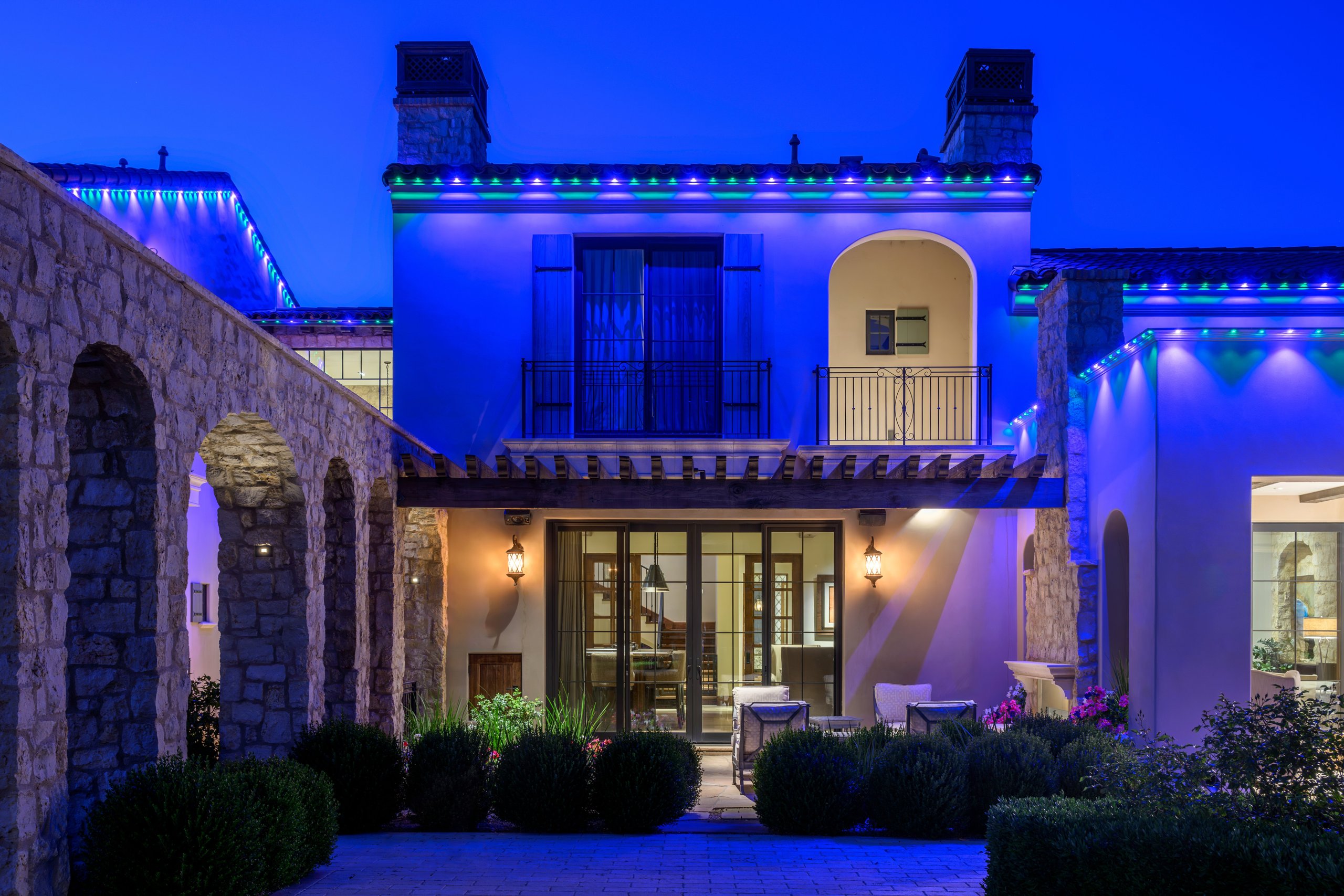 Blue and green permanent trim lighting on a Mediterranean stone estate with courtyard at dusk in Phoenix