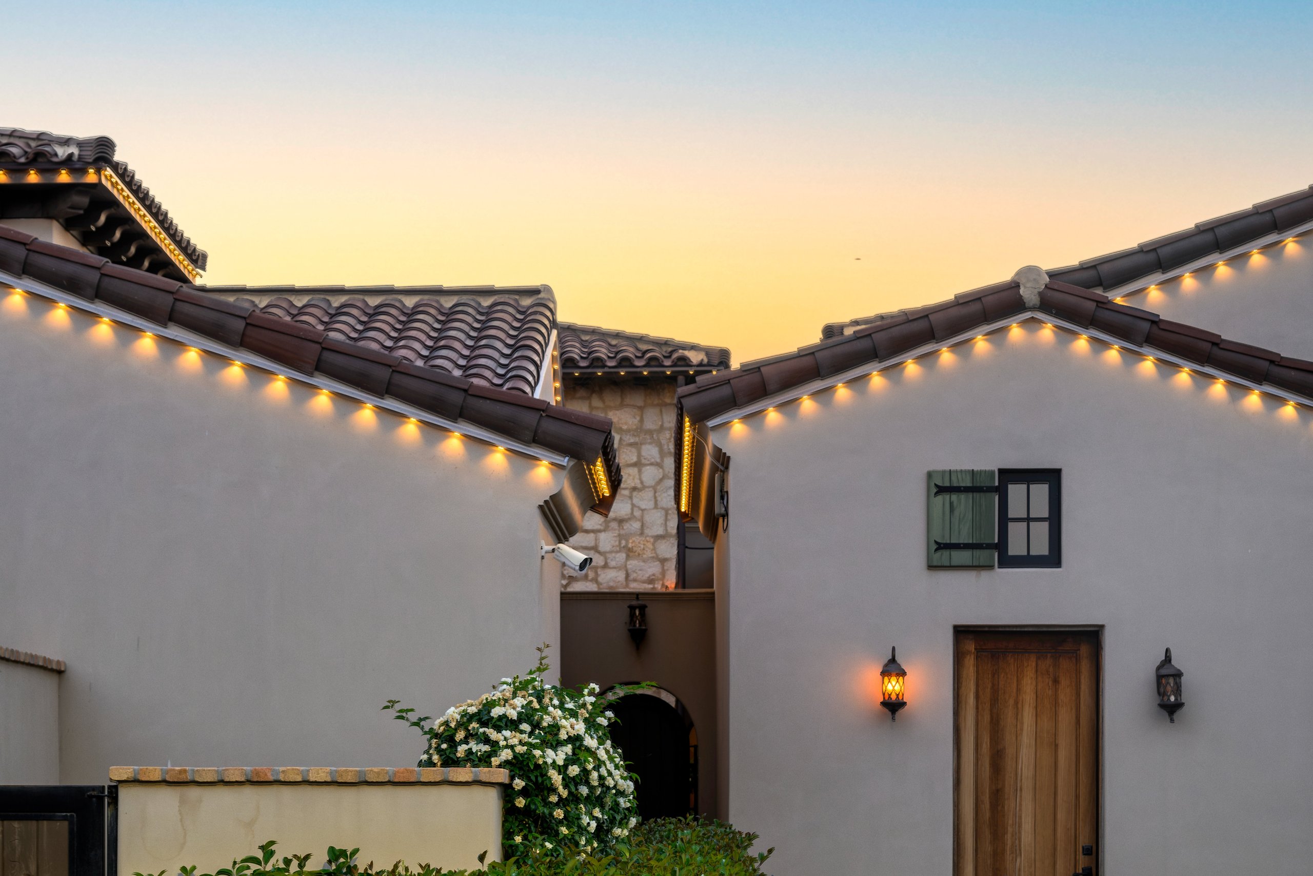 Warm white permanent trim lighting along the rooflines of a tile-roof stucco home at dusk in Phoenix